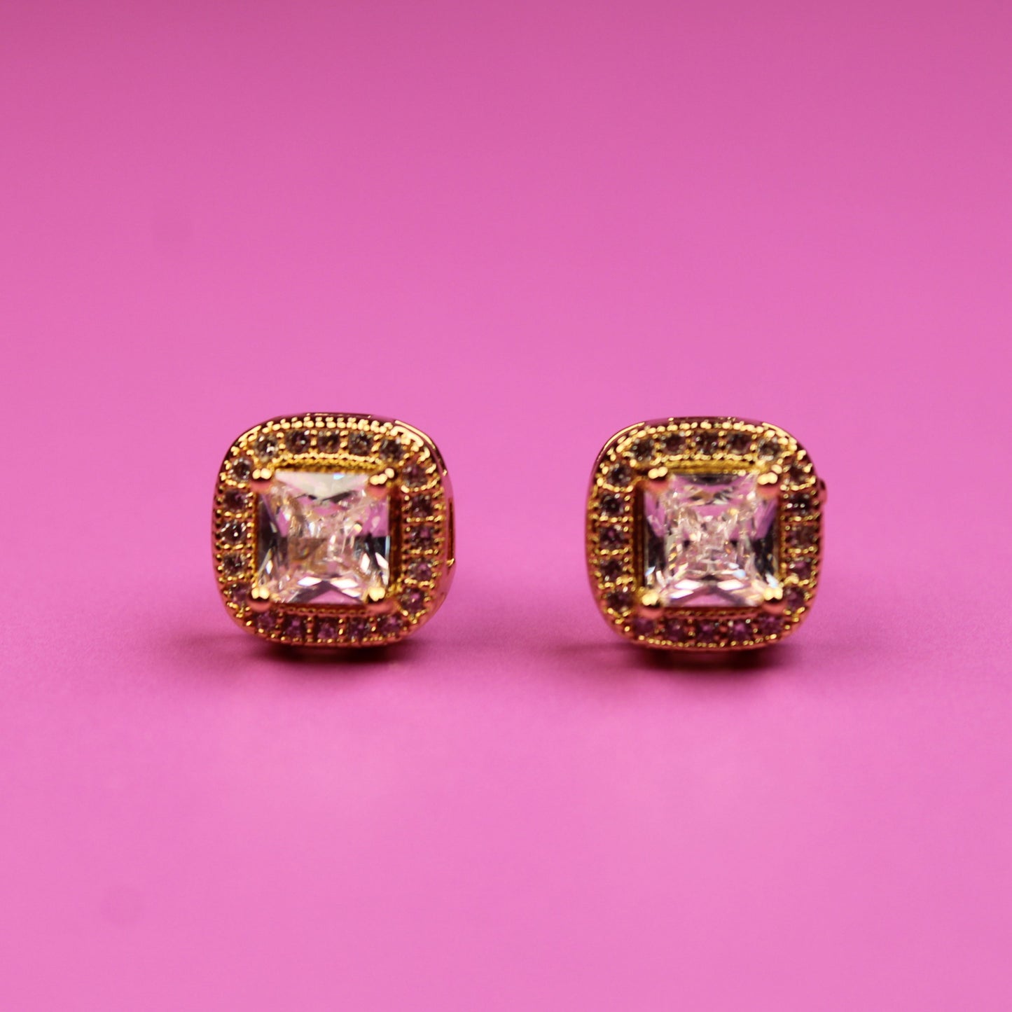 Gold earrings with square gemstones on a pink background
