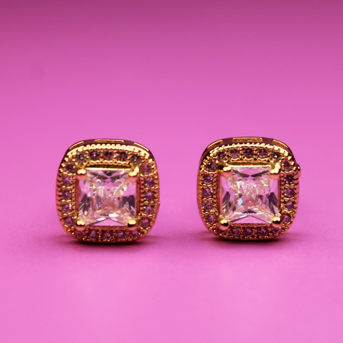 Pair of pink gemstone earrings with gold accents on a pink background