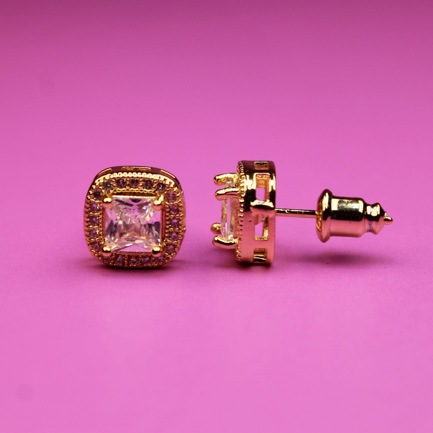 Gold earrings with pink gemstones on a pink background