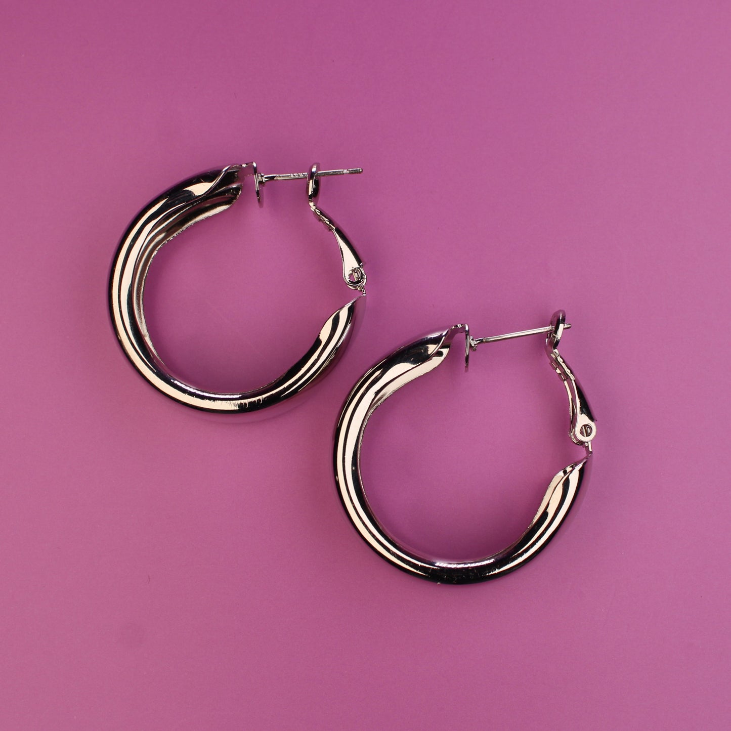 Pair of silver hoop earrings on a pink background