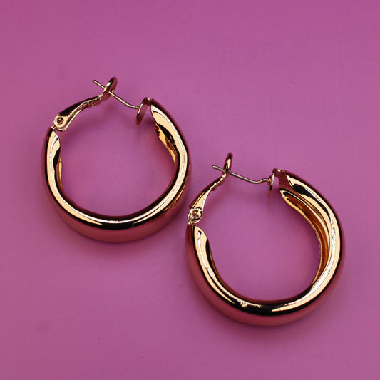 Gold hoop earrings on a pink background