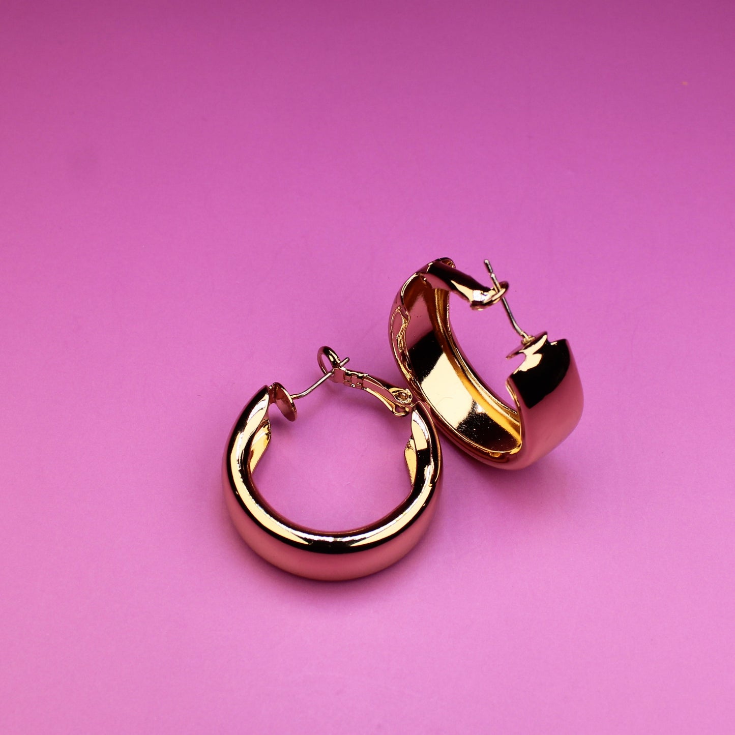 Gold hoop earrings on a pink background