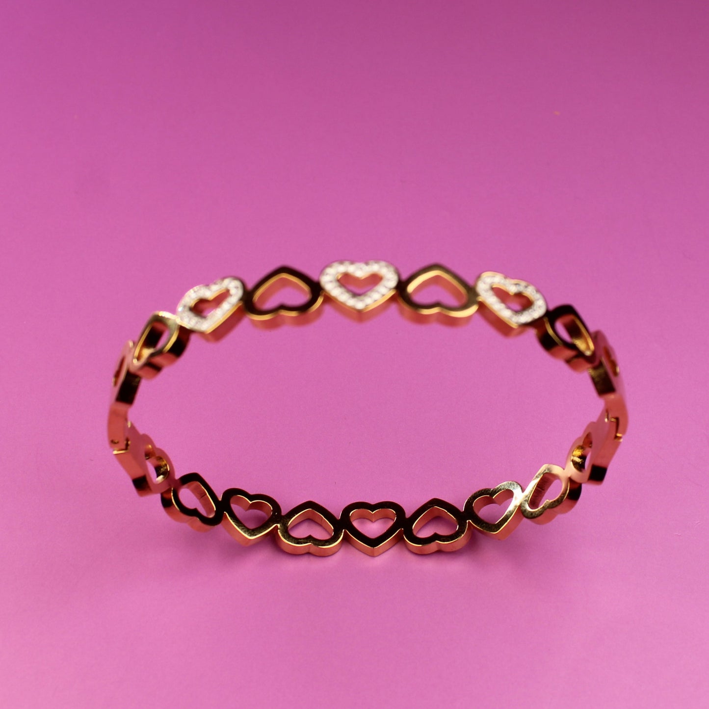 Gold bracelet with heart-shaped links on a pink background