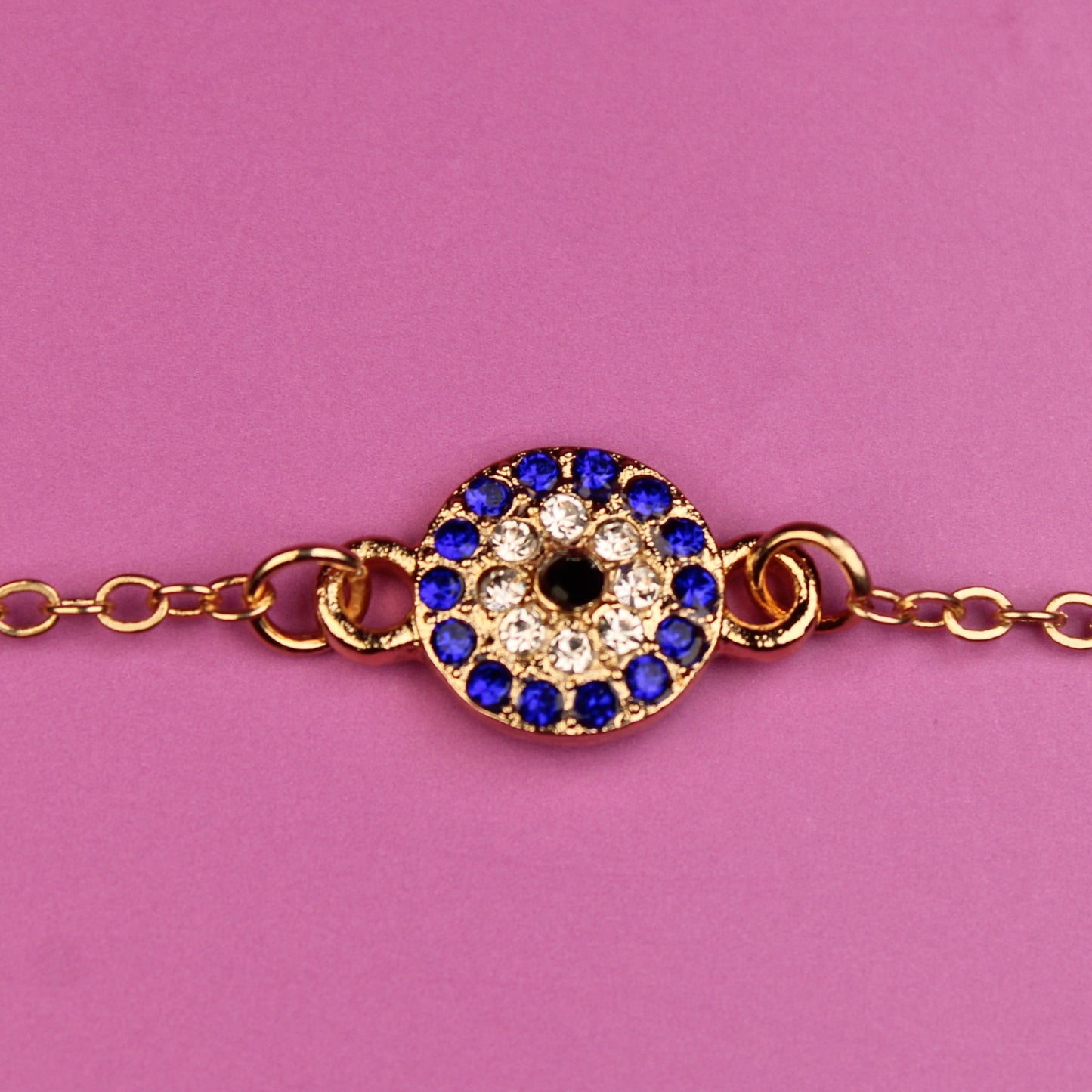 Gold bracelet with a blue and black gemstone on a pink background