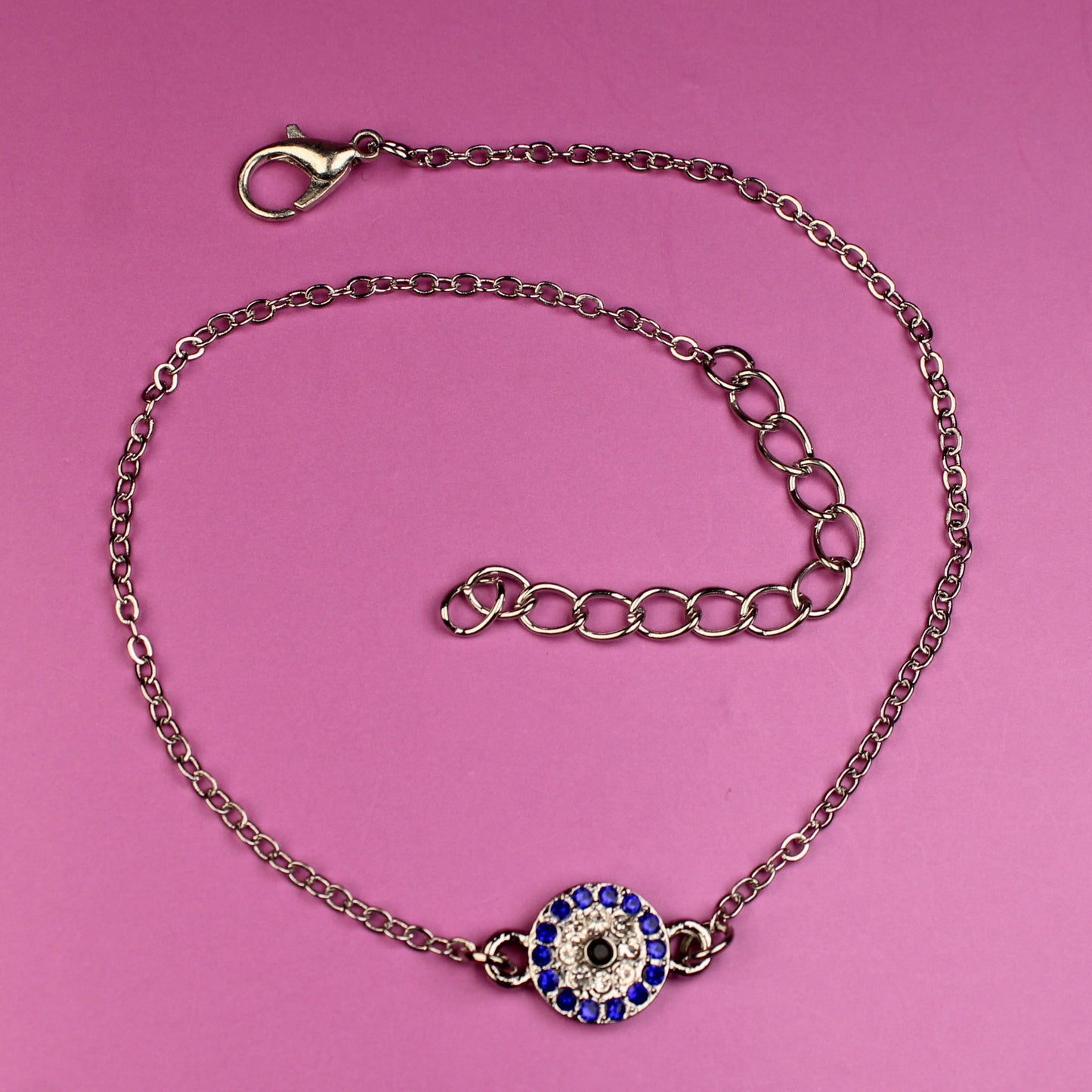 Bracelet with a blue and purple evil eye charm on a pink background