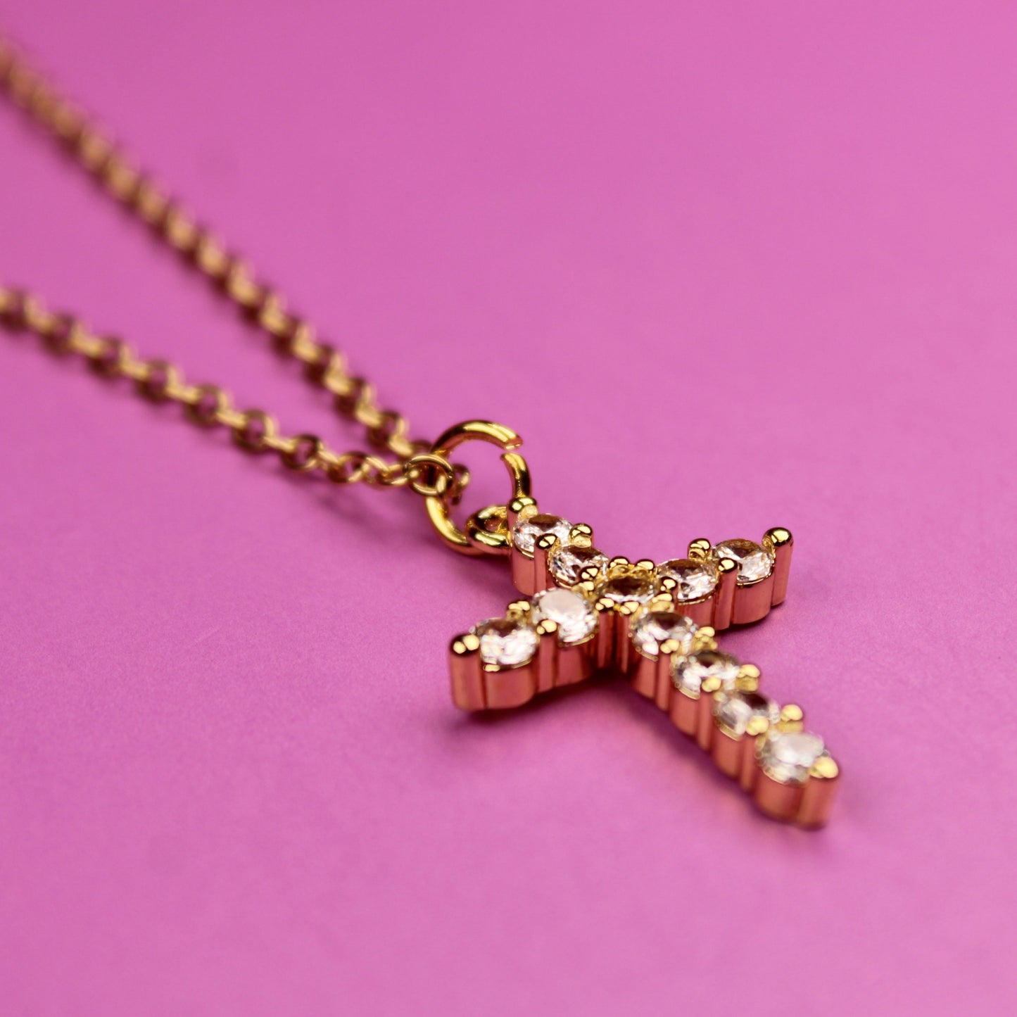 Gold cross necklace on a pink background