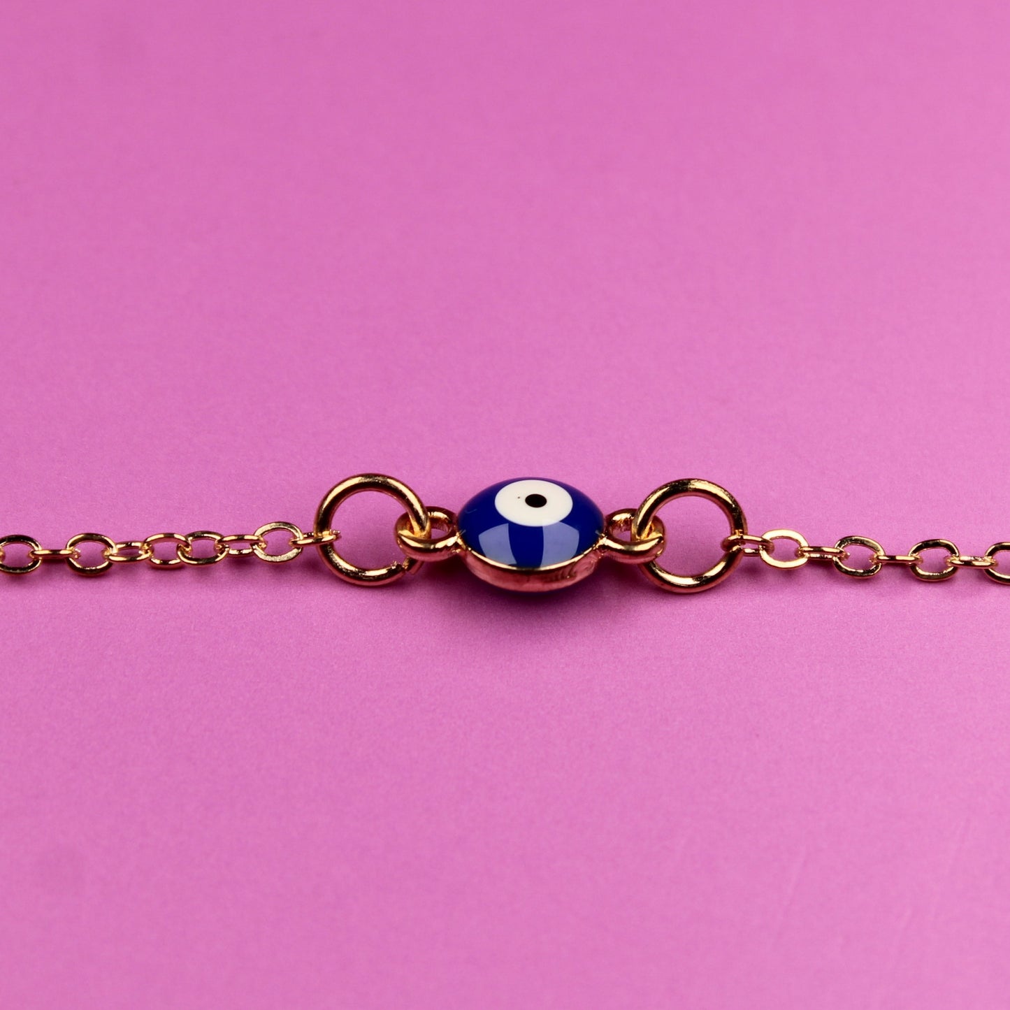 Bracelet with a blue evil eye charm on a pink background