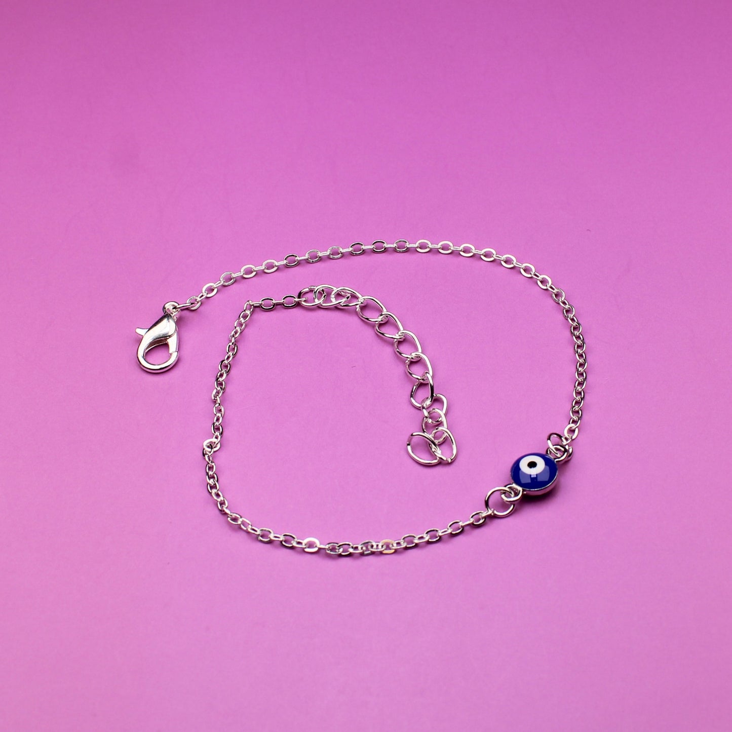 Silver bracelet with a blue evil eye charm on a pink background