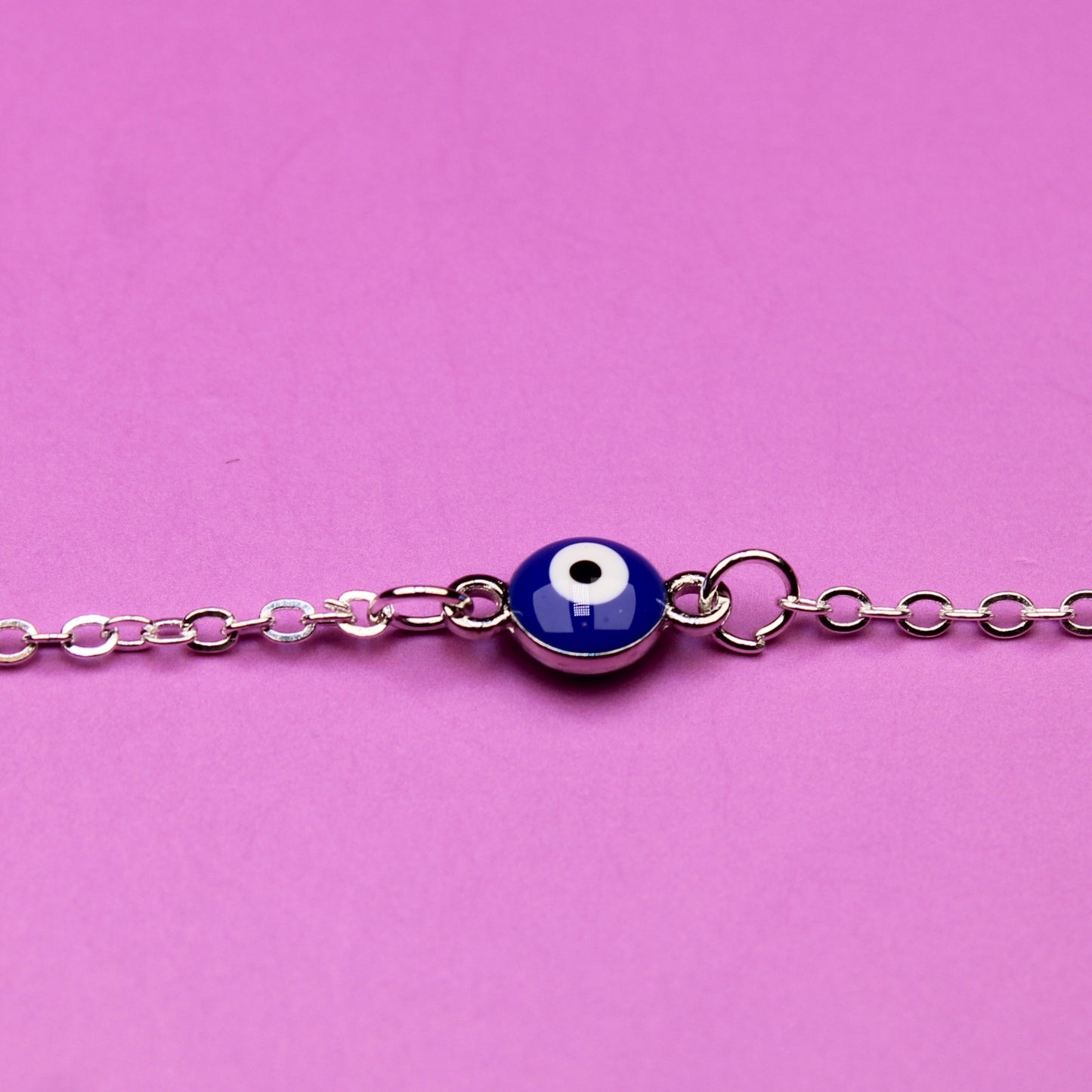 Silver bracelet with a blue evil eye charm on a pink background