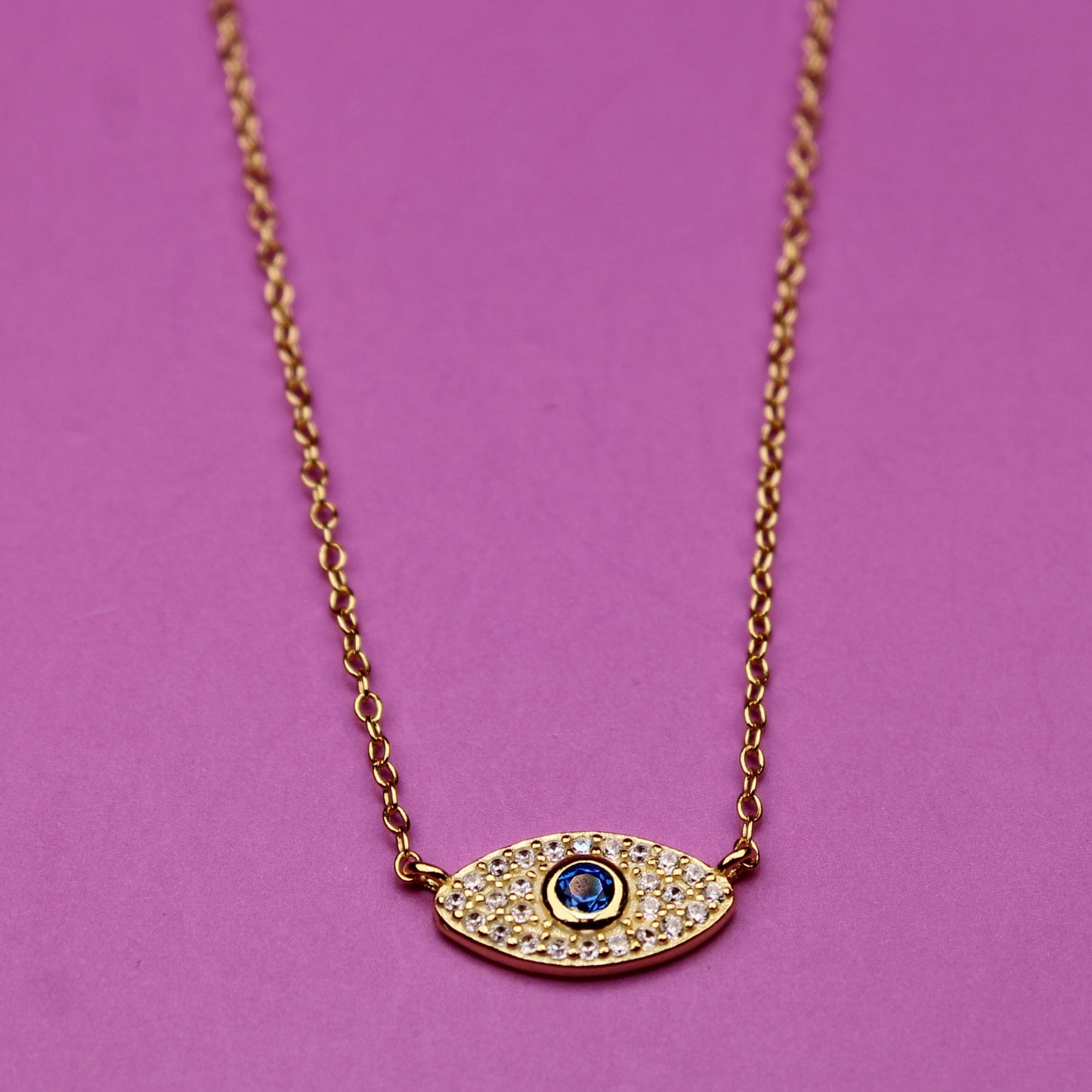 Gold necklace with an eye-shaped pendant on a purple background