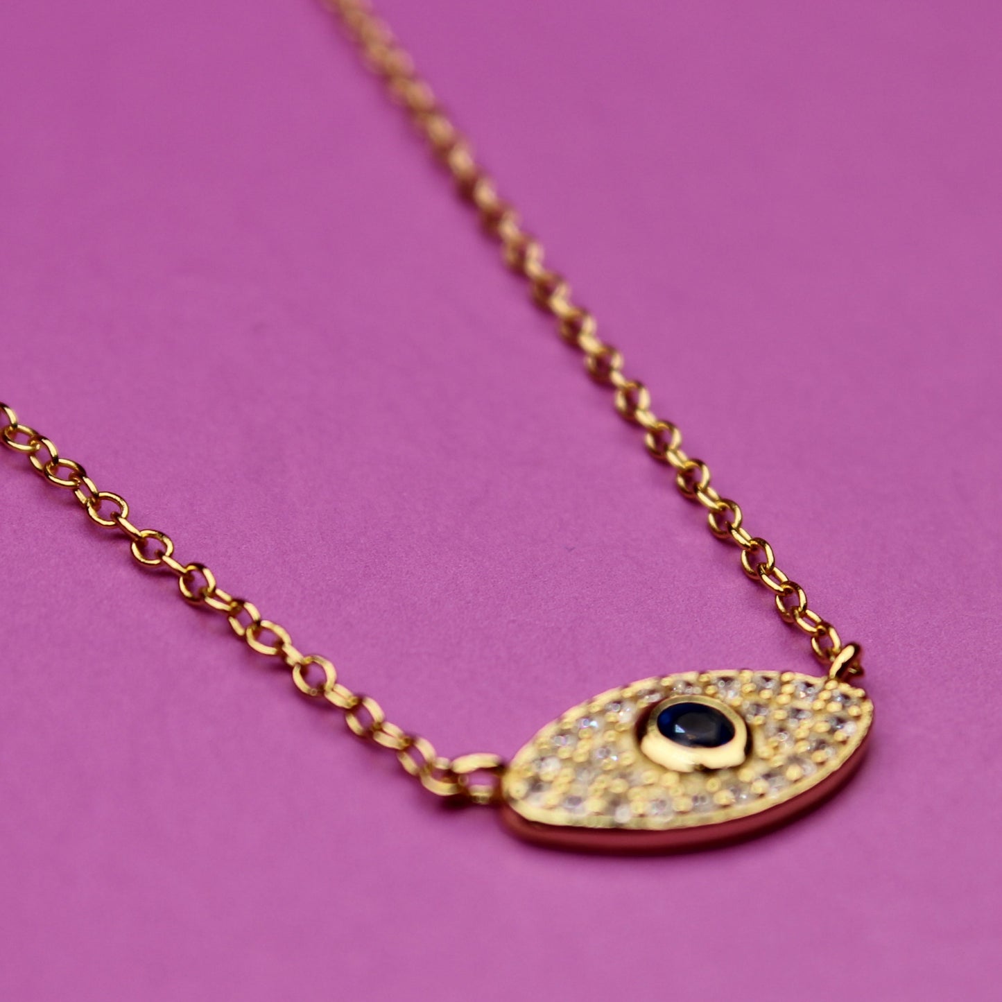 Gold necklace with an eye-shaped pendant on a purple background