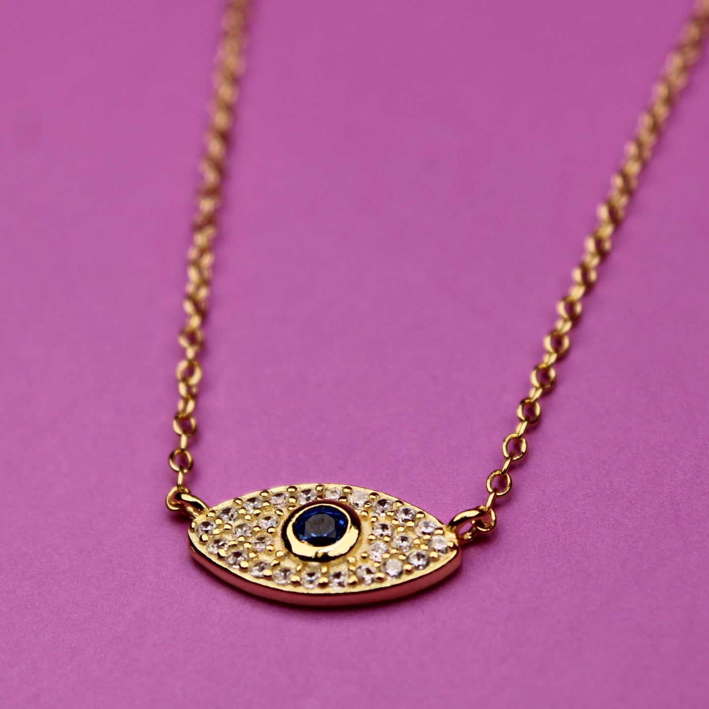 Gold necklace with an eye-shaped pendant on a pink background