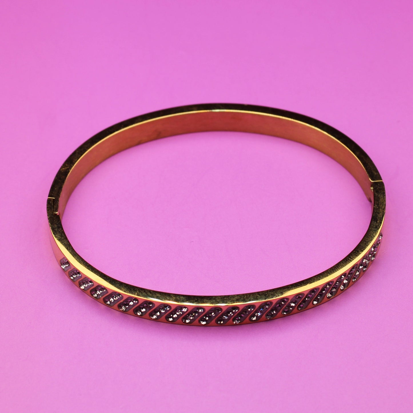 Gold bracelet with red stones on a pink background