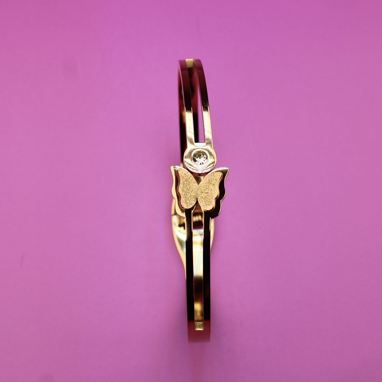Gold ring with a butterfly design on a pink background