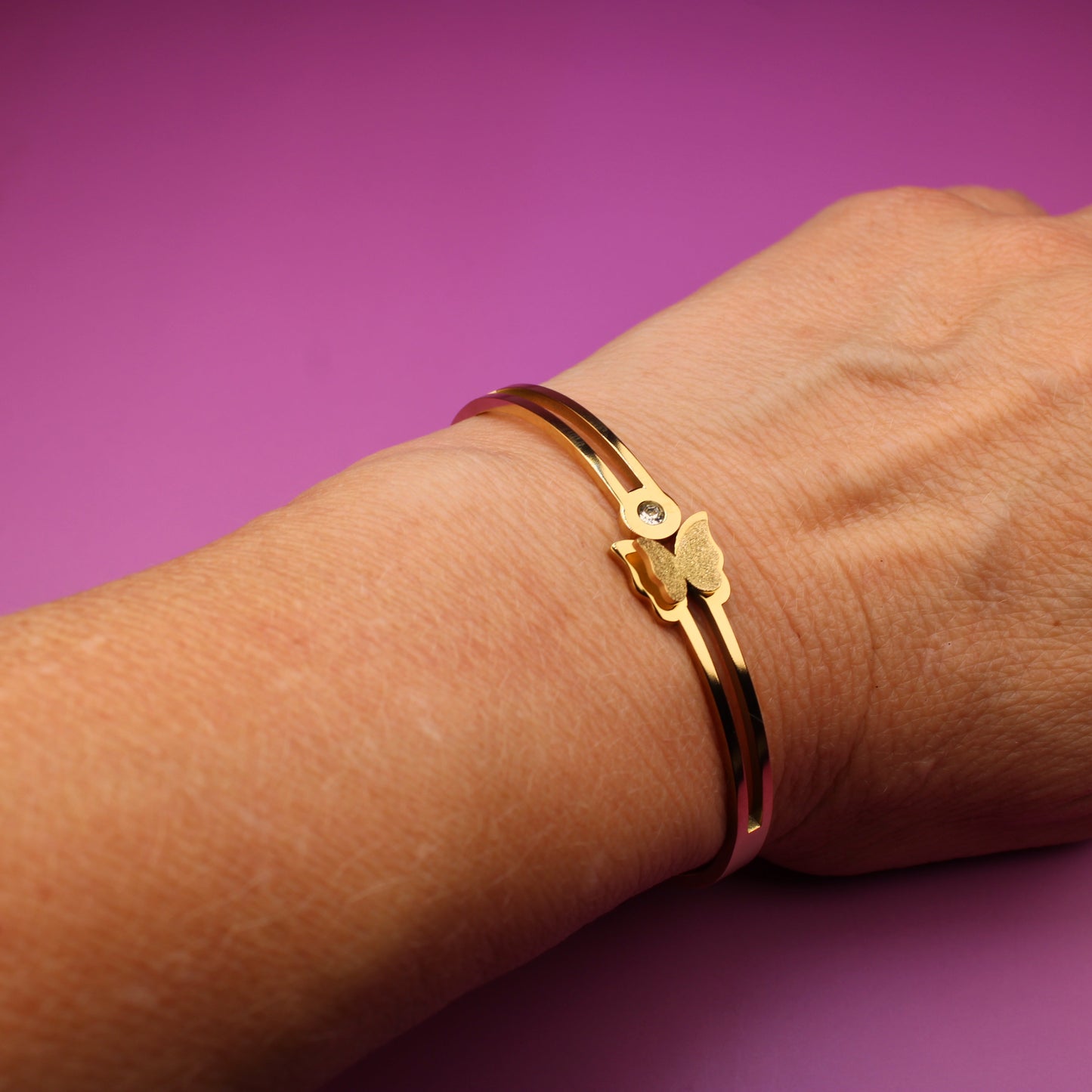 Hand wearing a gold bracelet on a purple background