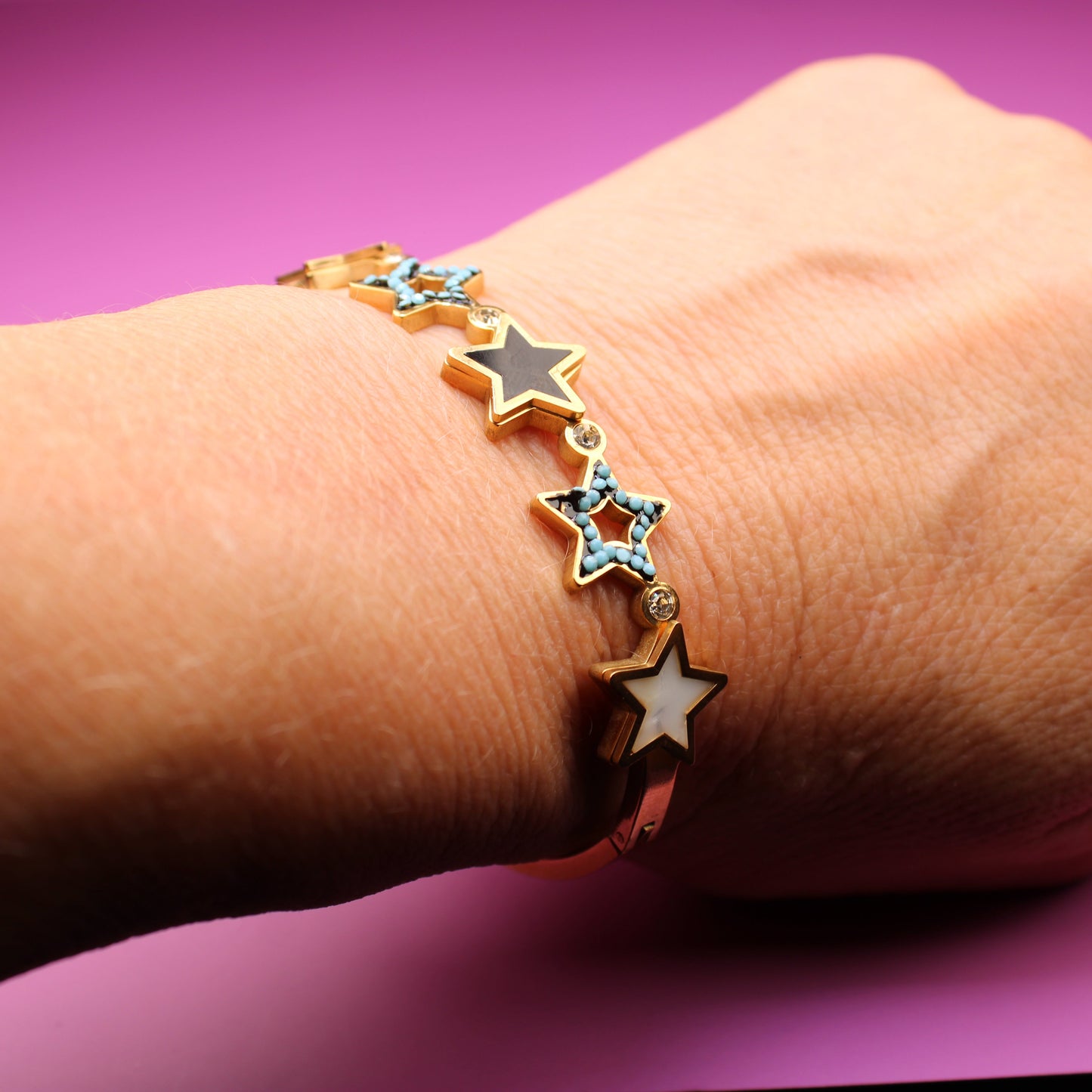 Hand wearing a bracelet with star-shaped charms on a purple background