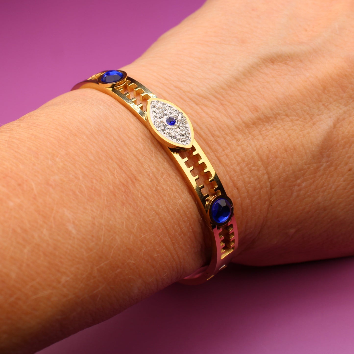 Gold bracelet with blue and green stones on a wrist against a purple background