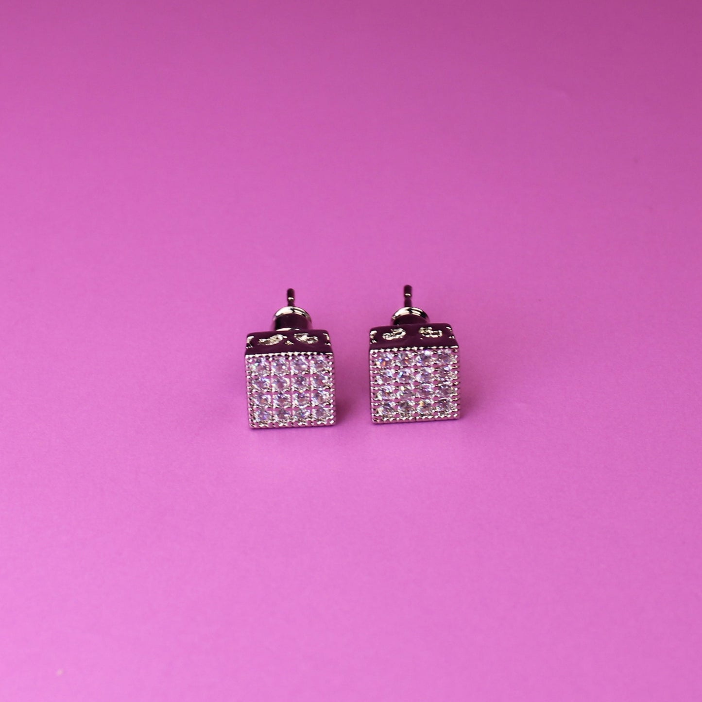 Pair of square earrings with small diamonds on a pink background