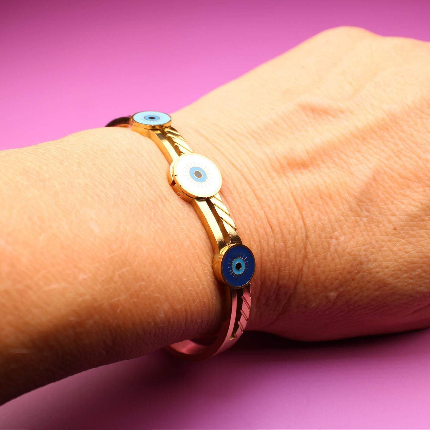 Gold bracelet with colorful beads on a wrist against a pink background