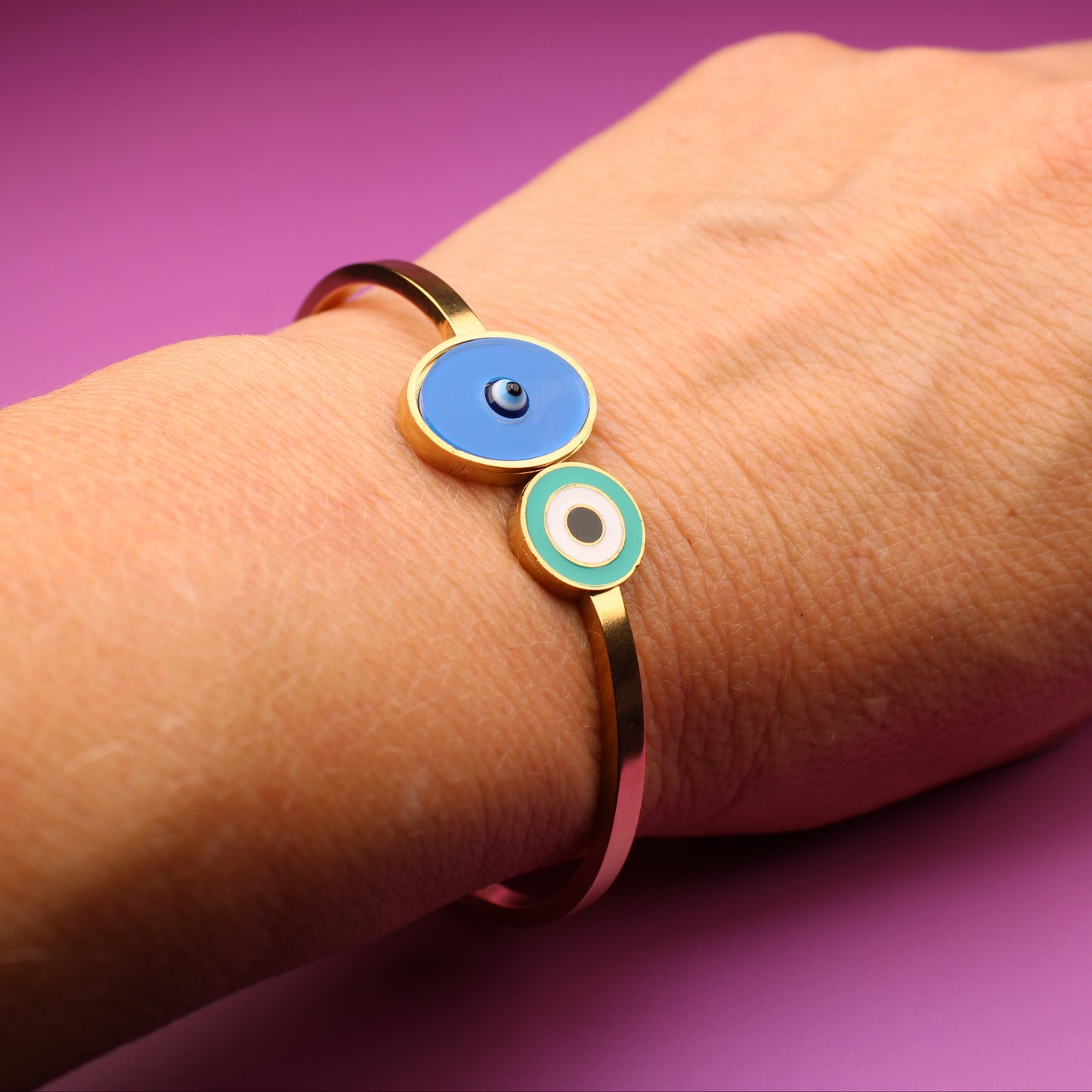 Hand wearing a gold bracelet with blue and green circular charms on a purple background