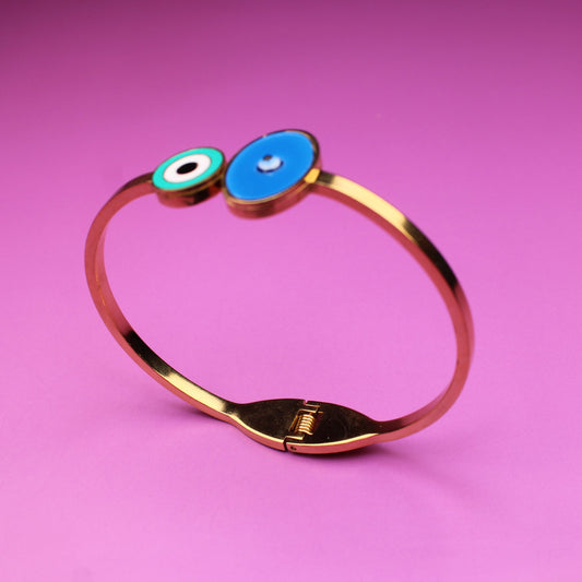 Gold bracelet with blue and green beads on a pink background