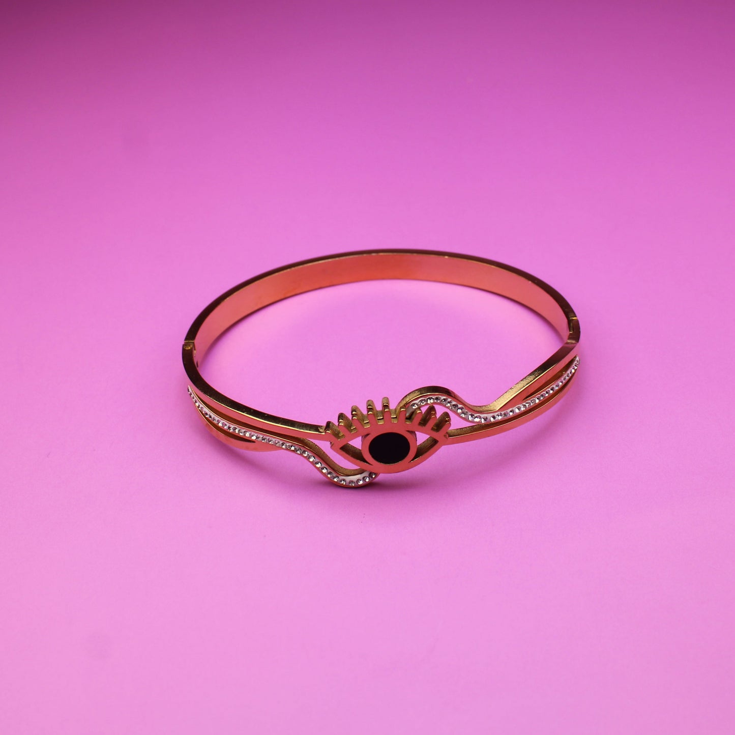 Rose gold bracelet with a black gemstone on a pink background