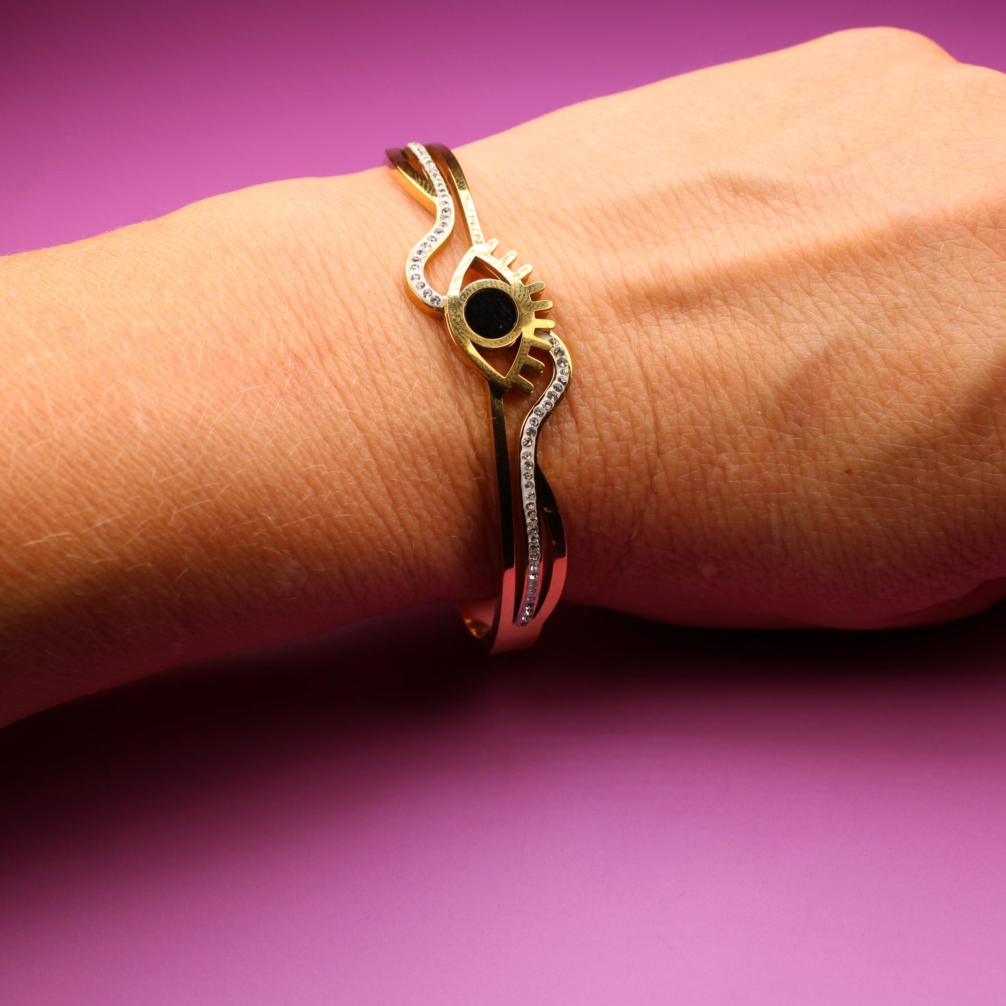 Gold bracelet with a black stone on a wrist against a purple background