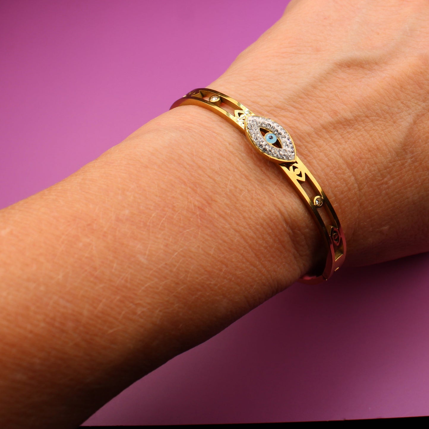 Hand wearing a gold bracelet on a purple background