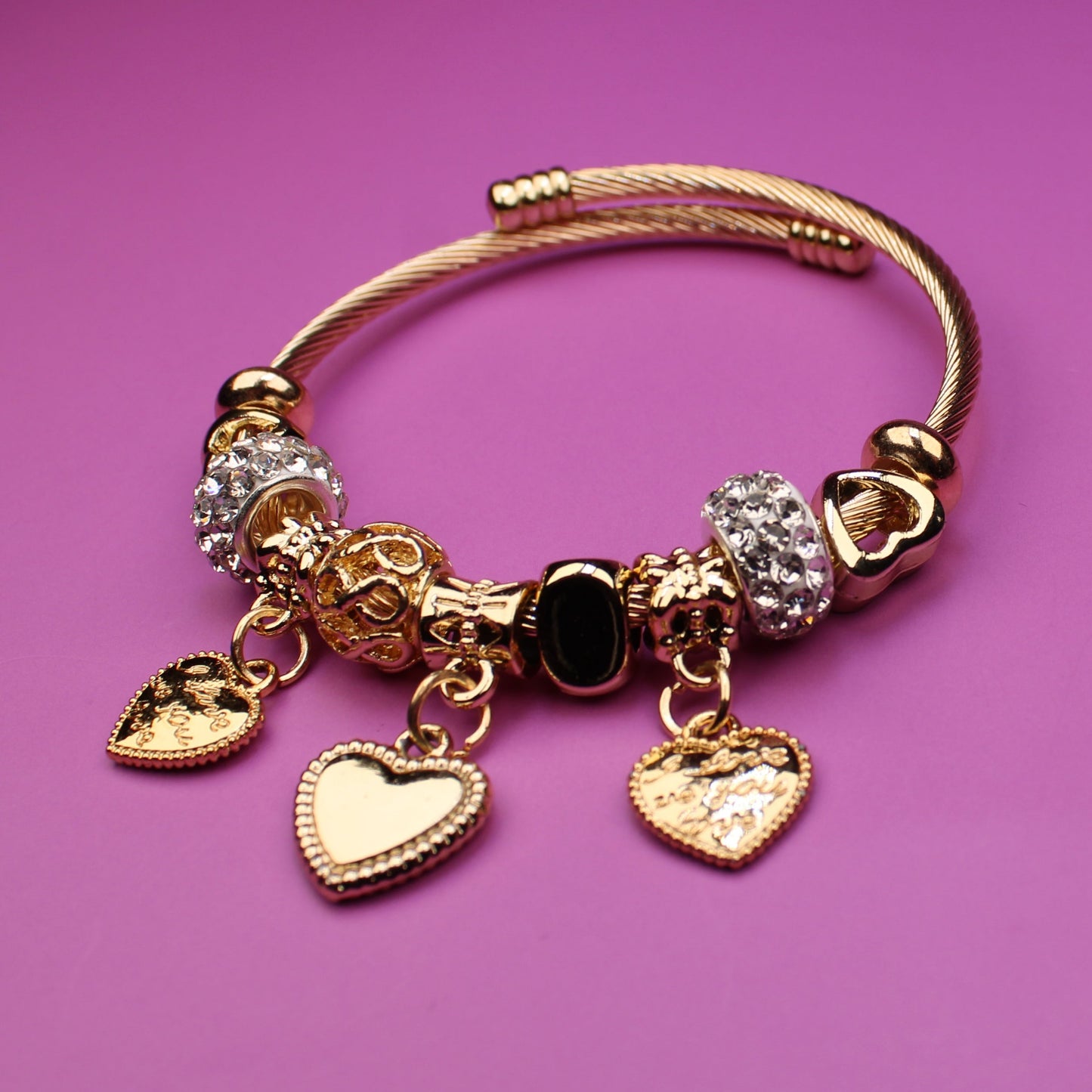 Gold bracelet with heart-shaped charms on a pink background