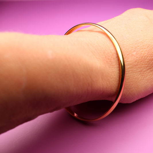 Hand wearing a gold bracelet on a pink surface