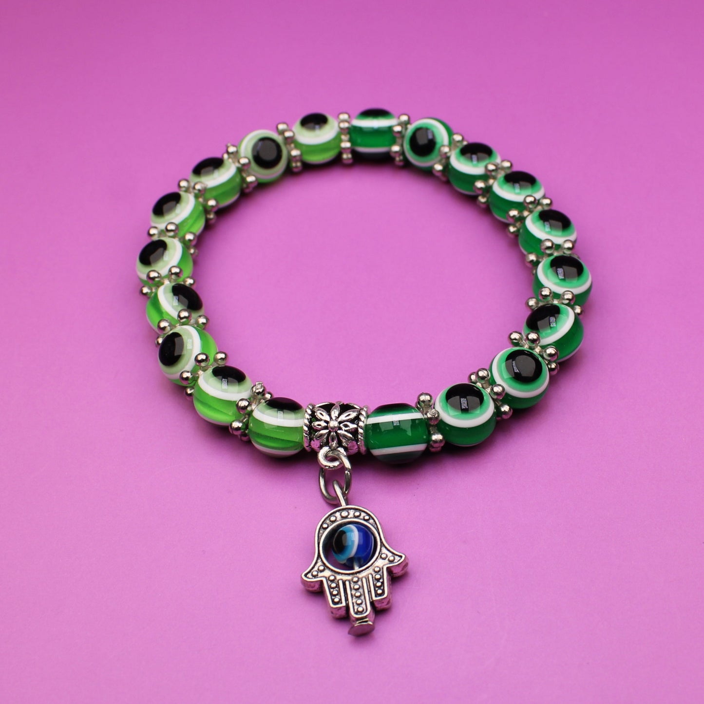 Green beaded bracelet with a Hamsa charm on a pink background