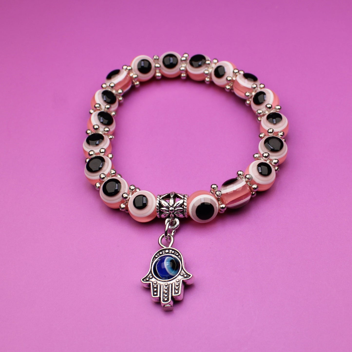 Bracelet with decorative beads and a hamsa charm on a pink background