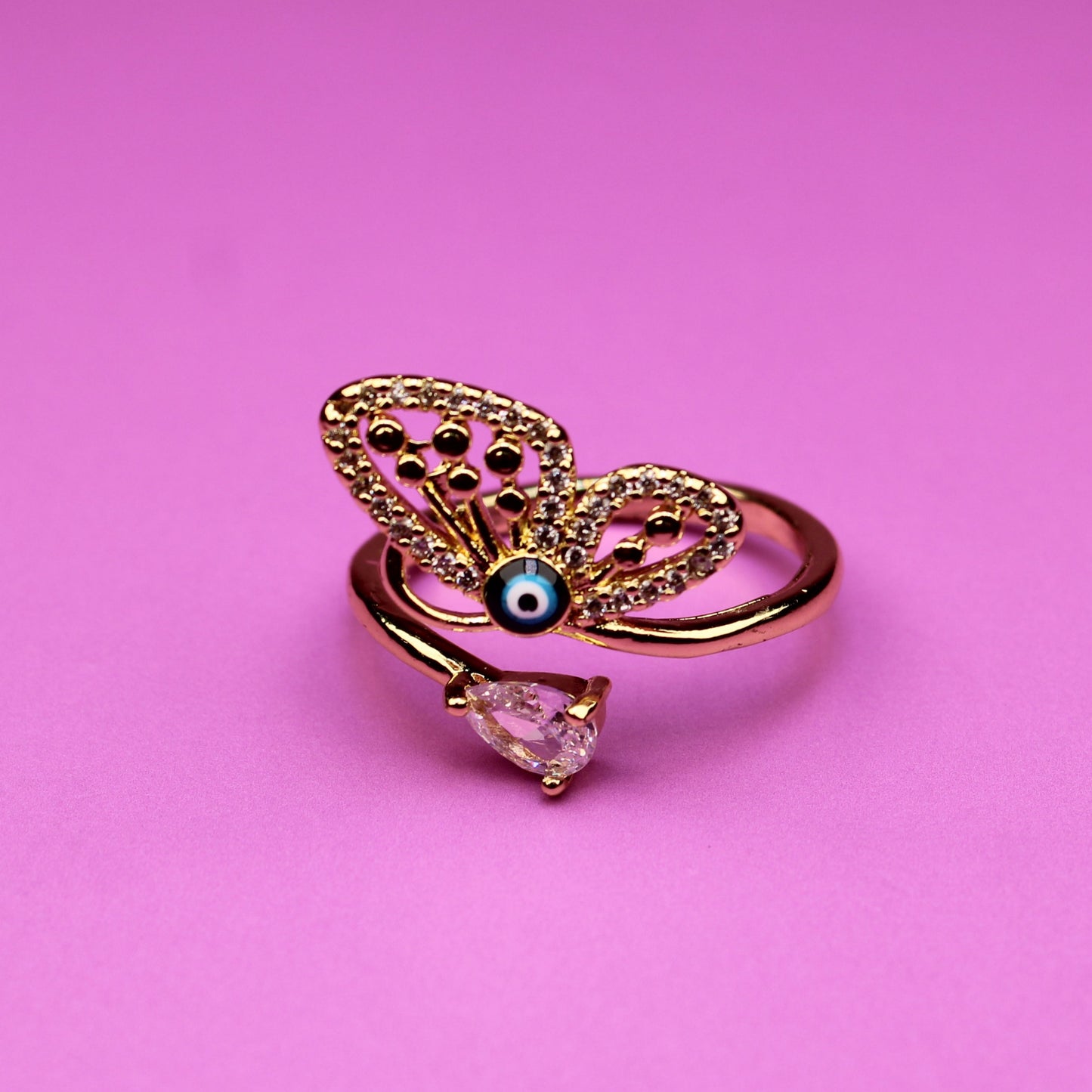 Gold butterfly ring with a pink gem on a pink background