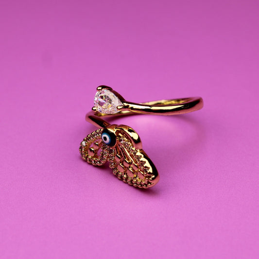 Gold ring with a heart-shaped pendant on a pink background