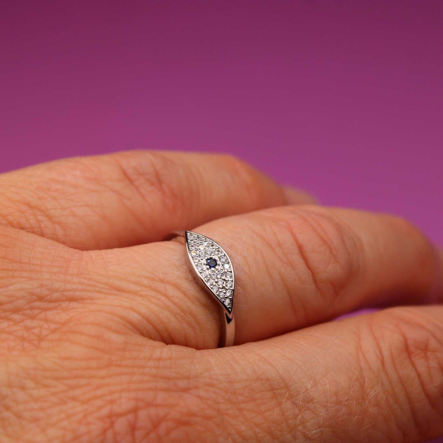 Silver ring with gemstones on a person's finger against a purple background