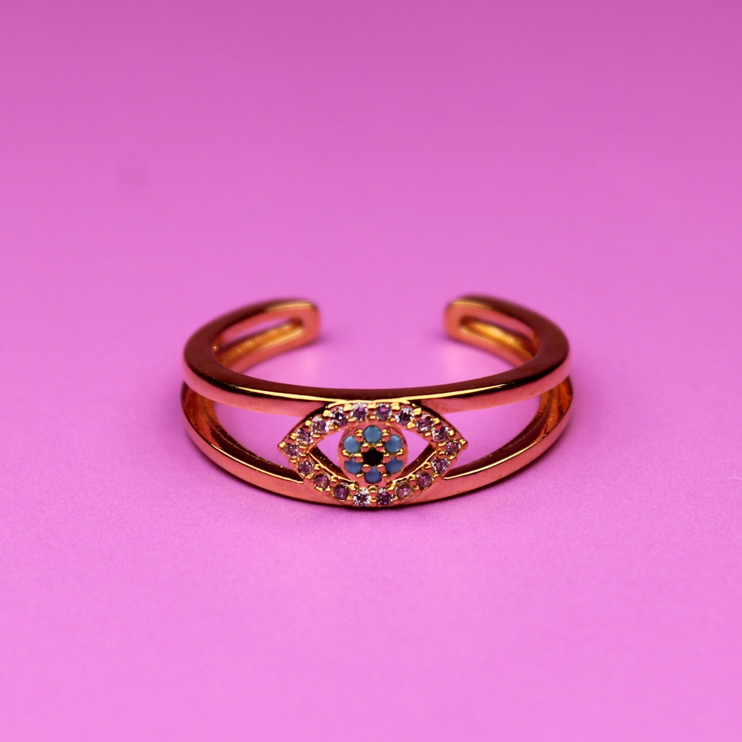 Gold bracelet with a colorful gemstone on a pink background