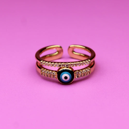 Gold ring with a blue eye design on a pink background