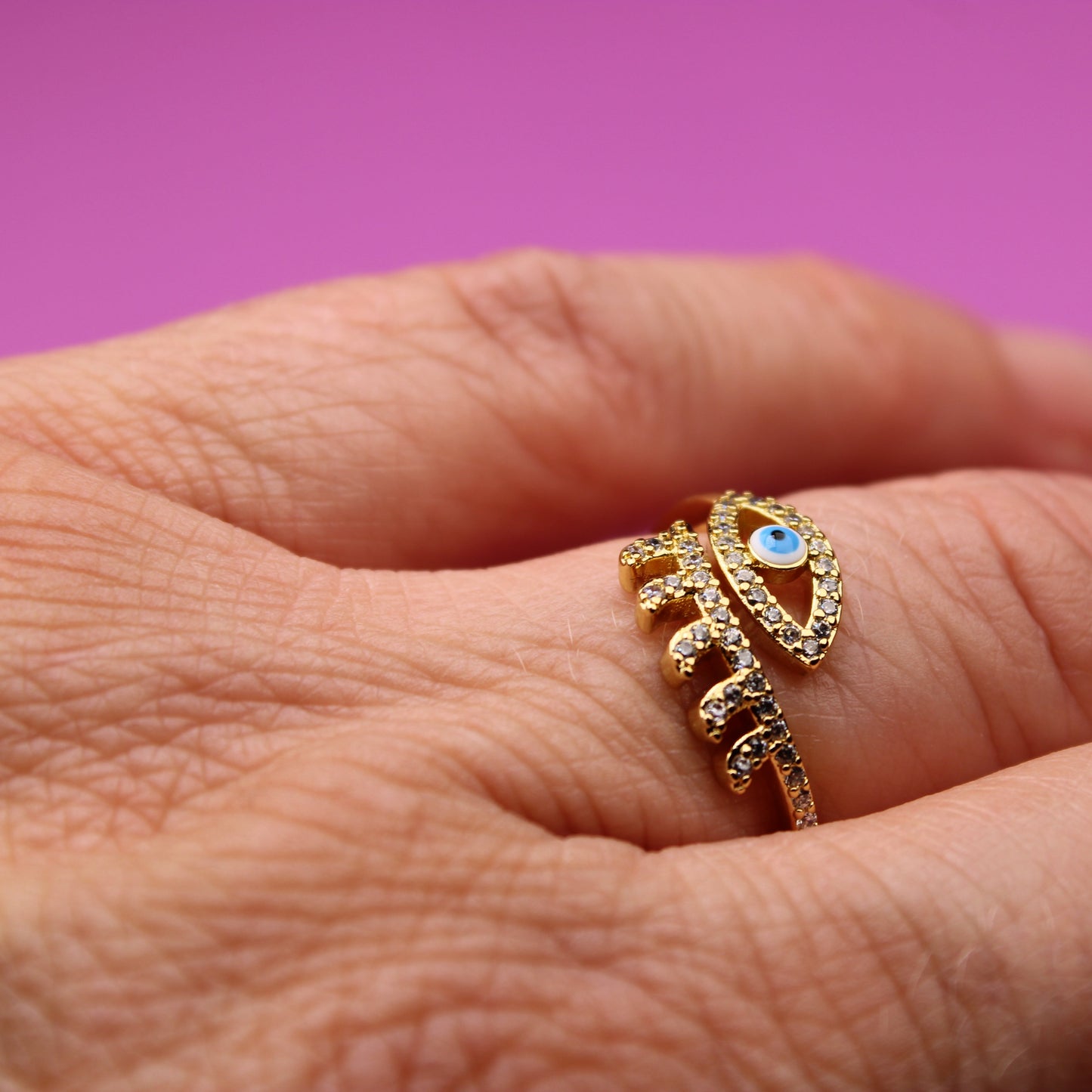 Gold ring with a blue gemstone on a person's finger against a pink background