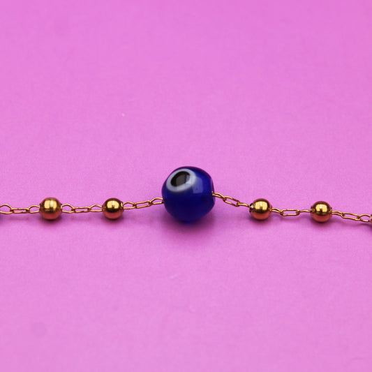 Bracelet with blue beads and gold chain on a pink background