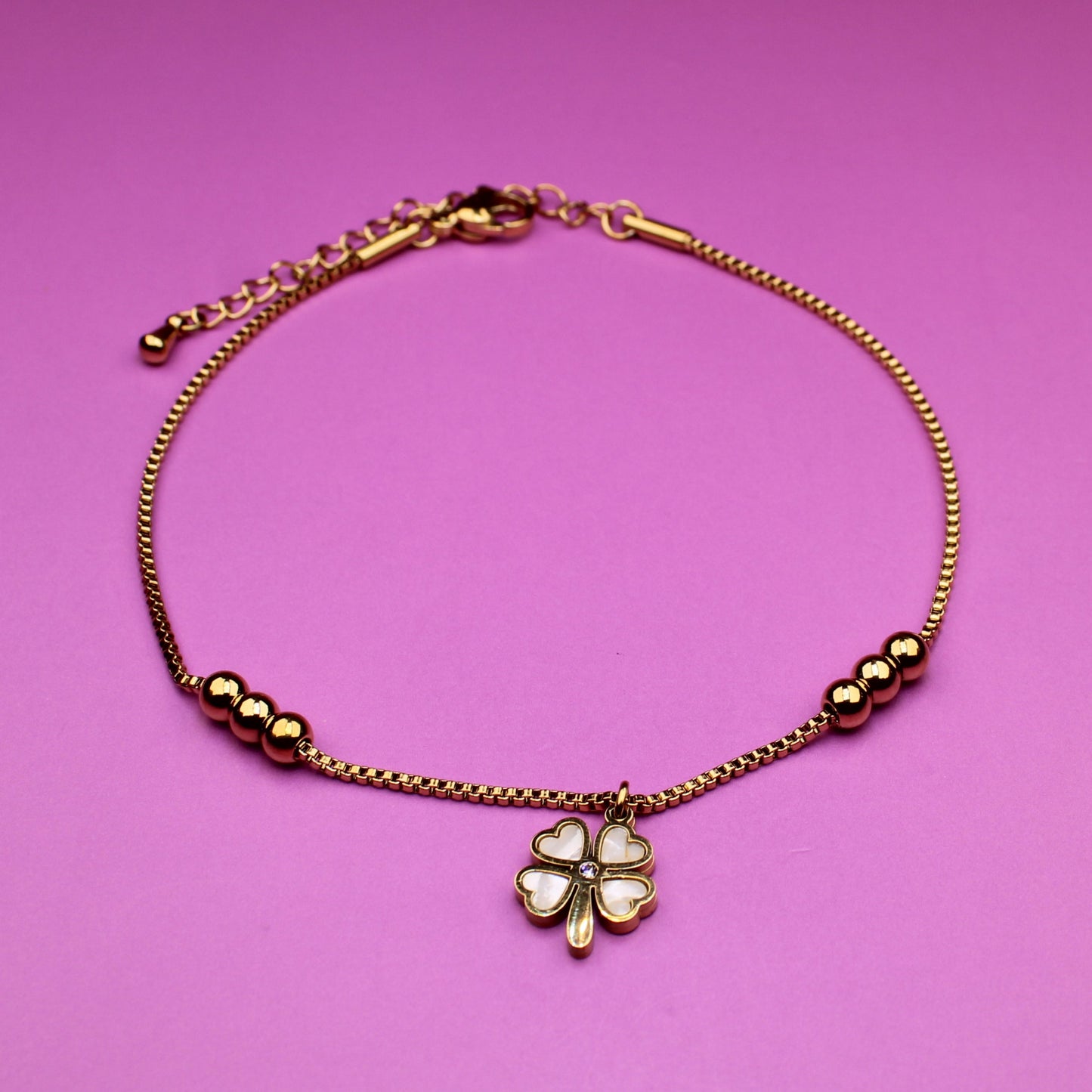 Gold bracelet with a clover charm on a pink background