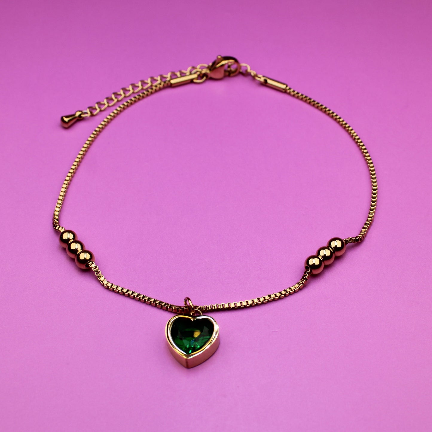 Gold bracelet with a heart-shaped green gemstone on a pink background