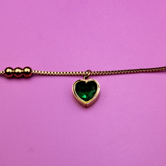 Bracelet with a heart-shaped green gemstone charm on a pink background
