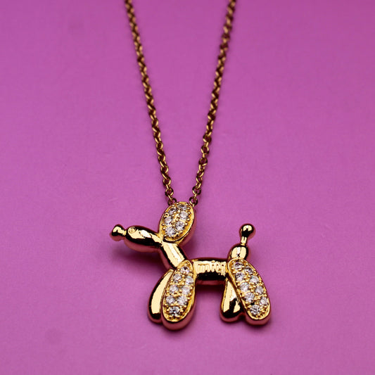 Gold dog-shaped pendant on a chain against a pink background