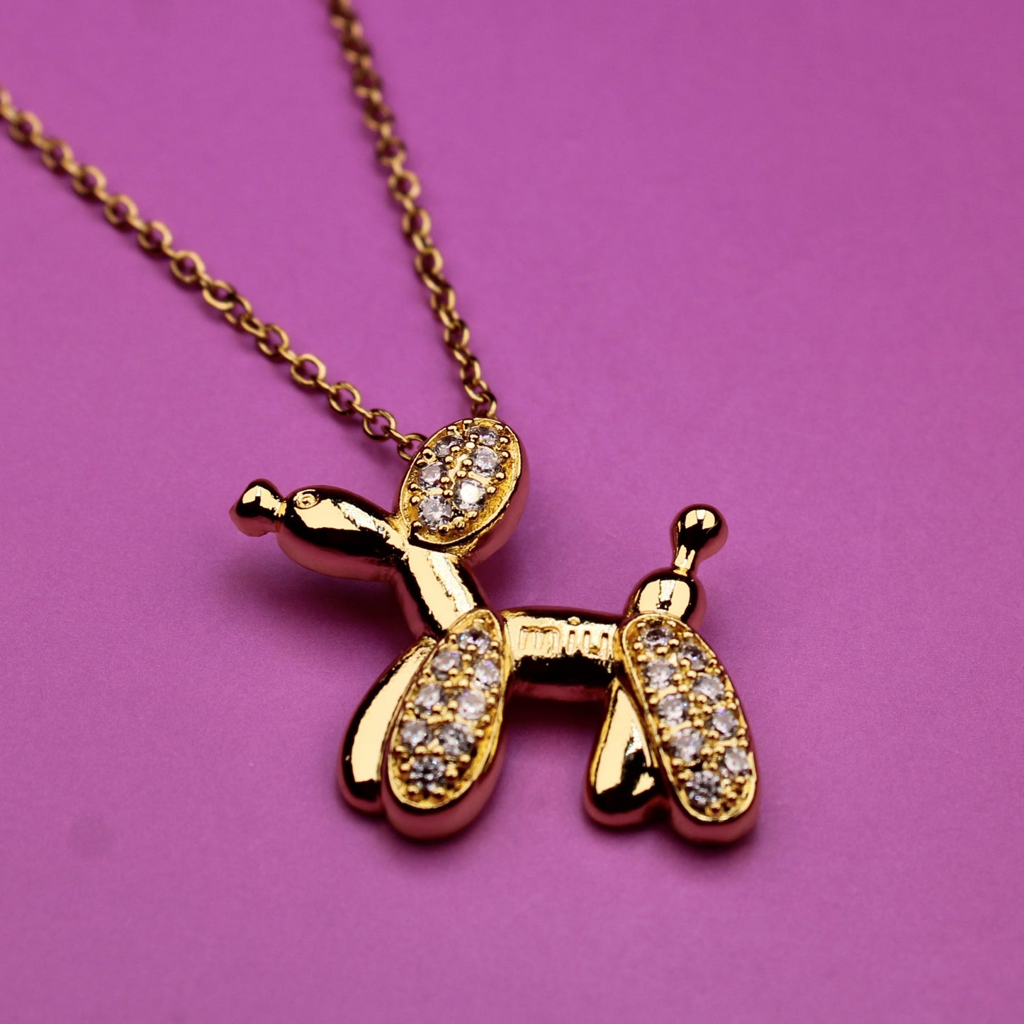 Gold dog-shaped pendant necklace on a pink background