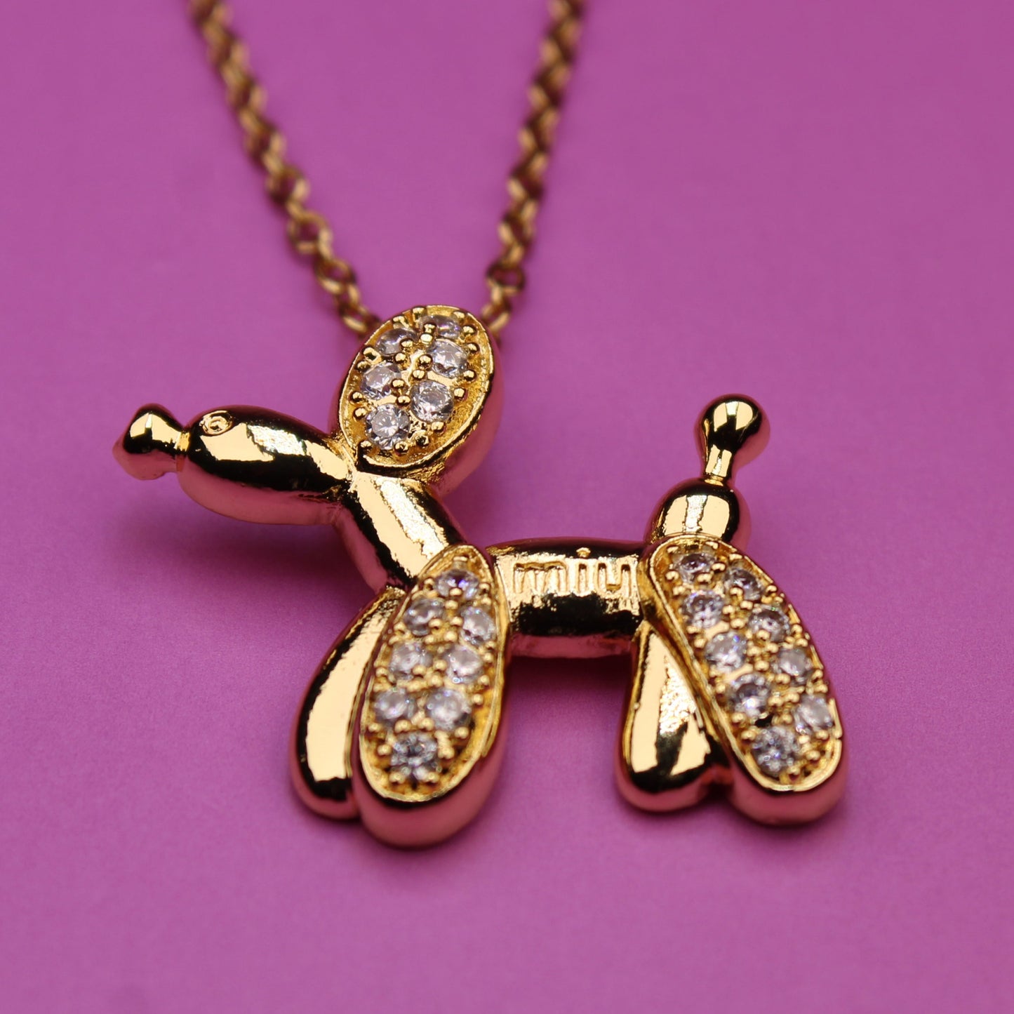 Gold balloon dog pendant necklace on a pink background