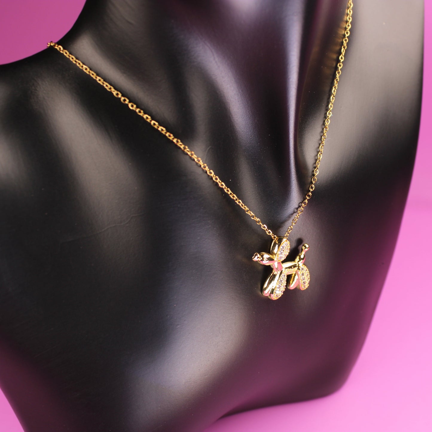 Gold necklace with a pendant on a black mannequin against a pink background