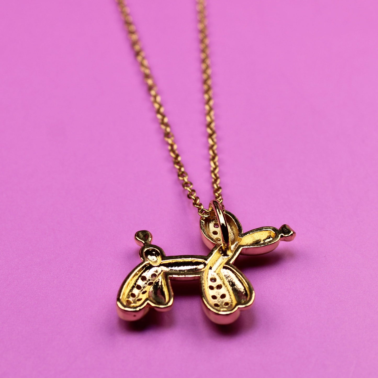 Gold necklace with a pineapple pendant on a pink background