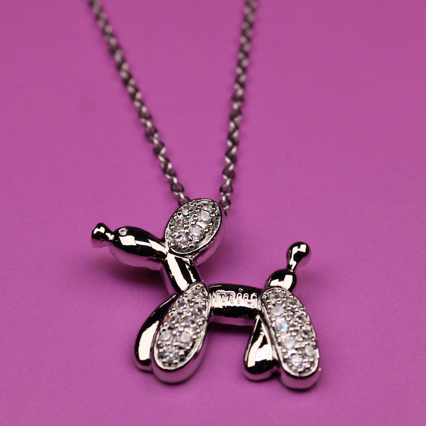 Silver balloon dog pendant necklace on a pink background