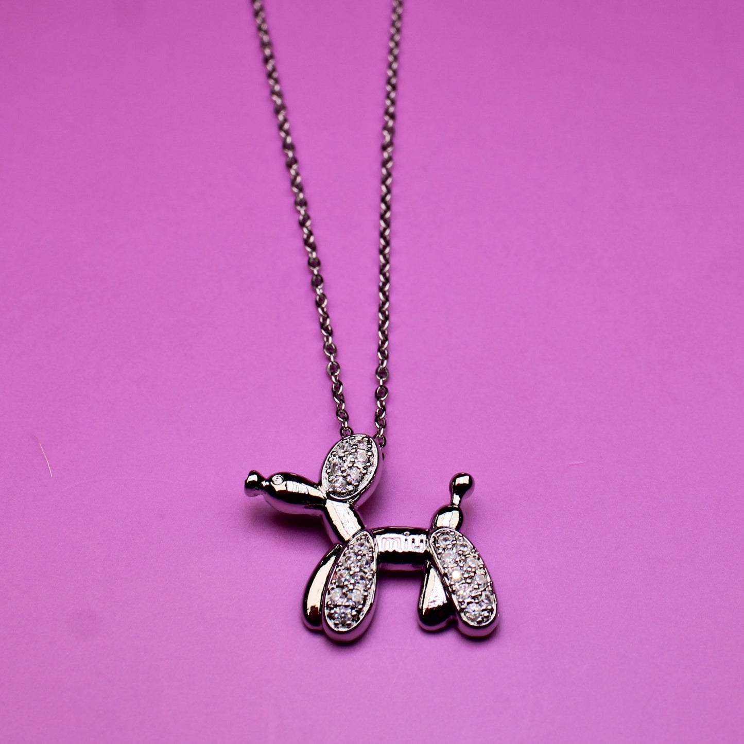 Necklace with a balloon dog pendant on a pink background