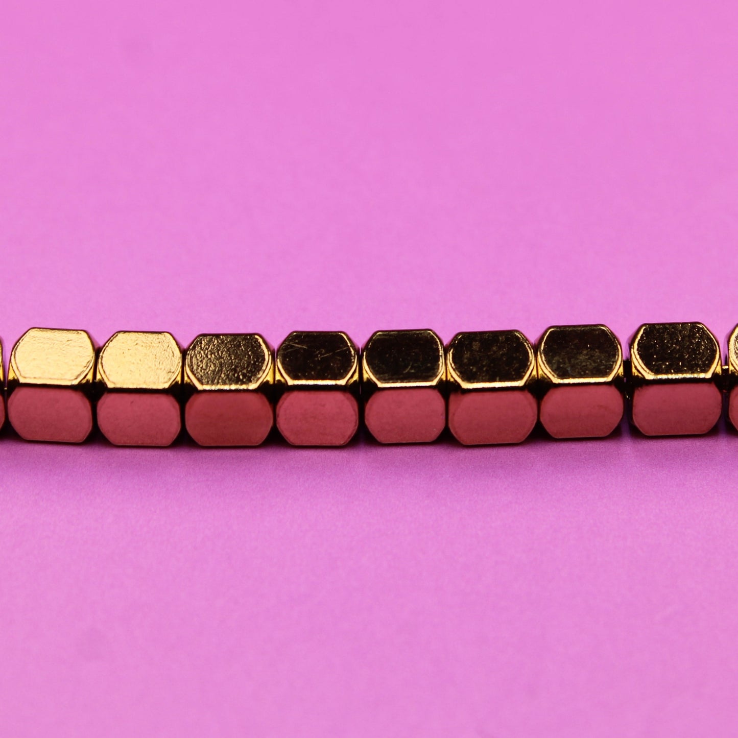 Bracelet with gold and red hexagonal beads on a pink background